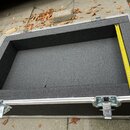 Otevřený transportní kufr s černým pěnovým vnitřkem a hliníkovými hranami. Uvnitř je přiložen žlutý natažený metr, který ukazuje délku přes 47 cm. Po…