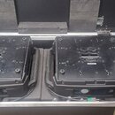 Dvě černé elektronické jednotky umístěné v transportním kufru s pěnovou výplní. Na horních stranách zařízení jsou viditelné technické popisky a štítk…
