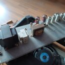 Fotografie zachycuje vnitřek elektronického zařízení, pravděpodobně zesilovače, s viditelnými elektrony a transformátory na šedém kovovém šasi. Na sp…