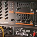 Černý mixážní pult s integrovaným zesilovačem značky YAMAHA, model EMX640 POWERED MIXER. Na spodní části je nalepený štítek s nápisem Extra Band. Zař…