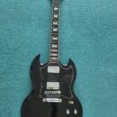 Černá elektrická kytara s dvojstupňovým snímačem a bílým lemováním kolem těla. Na hlavě hředu je zlatý nápis Gibson. Kytara má čtyři ovládací knoflík…