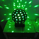 Černý kulatý disco projektor s otvory, který vyzařuje zelené světelné body na okolní stěnu a krabice. Zařízení stojí na dvou kartonech s nápisy Keter…