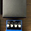 Na fotografii je modrý kytarový efekt s nápisem Compression Sustainer CS-3 a značkou BOSS. Pedal má čtyři bílé ovládací knoflíky s popisky LEVEL, TON…
