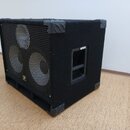 Černý basový reproduktor v bedně potažené látkou s kovovými rohy. Přední strana je kryta kovovou mřížkou, za kterou jsou vidět tři reproduktory. V do…