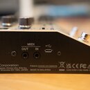 Zadní strana bílo-černého elektronického zařízení. Jsou zde vidět konektory MIDI OUT, MIDI IN a USB port. V dolní části je nápis Roland Corporation 2…