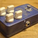 Modrý kytarový efekt s bílými oválnými knoflíky. Na horní straně je nápis MOJO JOJO, PAUL GILBERT OVERDRIVE a značka tc electronic. Přístroj vykazuje…