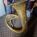 Mosazný železný nástroj, pravděpodobně tuba nebo euphonium. Povrch je v matném zlatavém odstínu s viditelnými škrábancem a opotřebováním laku. Na těl…