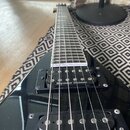 Černá elektrická kytara s hrazdovým hmatníkem. Na obou viditelných snímačích je bílý nápis Seymour Duncan. Povrch kytary vykazuje drobné prachové čás…