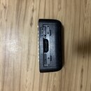 Zadní strana černého elektronického hudebního zařízení z plastu. Jsou zde vidět konektory, přepínač a slot pro kartu s nápisem "SD CARD". Povrch je v…