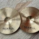 Dvě mosazné činely s jemným rýhováním povrchu. Oba mají černý nápis istanbul Agop Handmade cymbals from Turkey. Na levém činelu je navíc nalepený mal…