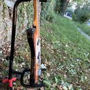Fotografie zachycuje elektrickou kytaru s černým tělem a světlou hnědou krkovnicí, umístěnou na černém stojanu. Na noze stojanu je viditelný nápis "H…