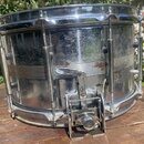 Kovový snare drum s chromovaným povrchem. Na korpusu jsou viditelné stopy koroze, oxidace a znečištění. Nástroj je vybaven chromovaným mechanismem pr…