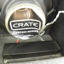 Fotografie zachicuje zadní stranu reproduktoru s černým magnetem a kovovým rámem. Na magnetu je nalepená kulatá nálepka s bílým nápisem CRATE a pod n…