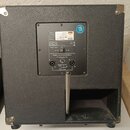 Zadní strana černého reproduktorového boxu s texturovaným povrchem a kovovými rohy. Na zadním panelu je štítek s nápisy: Power rms 300 Watts, Impedan…