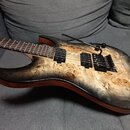 Elektrická kytara s tělem z masivu dřeva s výraznou přírodní kresbou a žlutohnědým povrchem. Nástroj má dva černé humbuckery, černý trestlový most s…