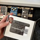 Bílá krabička s černým štítkem, na kterém je bílý nápis Compressora a logo Keeley Electronics. Na štítku jsou dále texty ENGINEERED AND MADE IN EDMON…