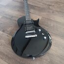 Černá elektrická kytara s tvarem připomínajícím model Les Paul. Nástroj má dva humbuckery, Tune-o-matic můstek a dvě ovládací knoflíky. Povrch je les…