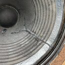 Detailní záběr na černý reproduktorový membránu s koncentrickými vrstvami. V dolní části je viditelná výrazná trhlina v materiálu membrány. Povrch vy…