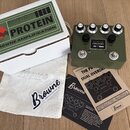 Na fotografii je kytarový efekt v zeleném kovovém šasi s nápisem PROTEIN a logem BROWNE AMPLIFICATION. Pedál má čtyři ovládací knoflíky, dva přepínač…