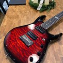 Elektrická kytara s červeným plamenovitým povrchem a černým okrajem. Na hmatníku je viditelné logo značky Ibanez. Kytara má dva humbuckery, pětiposit…