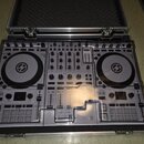 Stříbrný DJ 컨트롤러 umístěný v otevřeném hliníkovém kufru s černou pěnovou výplní ve víku. Zařízení má dva velké jog-wheels, faderové posuvníky a početn…
