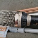 Dynamický mikrofon s kovovou síťkovou hlavou a černým tělem. Na stříbrném prstenci je vyrazen nápis UM 70 a vedle něj jsou tři symboly (nekonečno, vl…