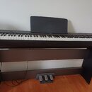 Digitální piano v černé barvě s bílými a černými klávesami, umístěné na matchingovém černém stojanu. Součástí je černý notový pouzdro a pedálová jedn…