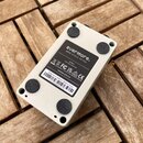 Bílá obdélníková krabička s nápisem evermore. a UAFX STUDIO REVERB. Na spodní straně jsou čtyři gumové nožičky a štítek s textem: "Designed in Califo…