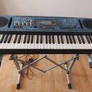 Tmavě modrý digitální klavír značky YAMAHA s modelem DTX. Nástroj je umístěn na stříbrném X-kovém stojanu. Na ovládacím panelu jsou viditelné knofíky…