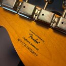 Záběr na zadní stranu hlavy kytary z přírodního dřeva s chromovanými ladičkami. Na dřevě je černý nápis Designed and Backed by Fender®, Crafted in In…