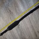 Černý popruh na hudební nástroj z textilního materiálu s širší středovou částí. Popruh je položen vedle žlutého skladovacího metru na šedé podlaze. N…