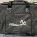 Černá textilní přepravní taška s dvěma rukojtěmi a předním zipovým přihrádkou. Na přední straně je bílý nápis Palmer pedalbay s doprovodnou grafikou…
