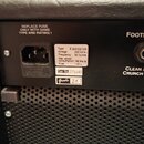 Detail zadní strany černého kytarového zesilovače. Je zde vidět napájecí konektor s nápisem REPLACE FUSE ONLY WITH SAME TYPE AND RATING ! a vstup FOO…