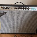 Kytarový kombo zesilovač s černým krytím a stříbrnou síťovkou. Na horním ovládacím panelu jsou nápisy CUSTOM a VINTAGE, značka Fender na přední stran…