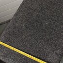 Obdélníkový předmět potažený tmavě šedým, texturovaným kobercovým materiálem. Přes předmět je položen žlutý skladací metr, který ukazuje šířku přibli…
