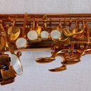 Detailní záběr na mechanismus zlatého saxofonu. Nástroj má lesklý povrch a bílé perleťové klapky. Na fotce nejsou žádné viditelné značky ani nápisy.