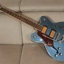Modrá polodupatá elektrická kytara s hnědým hmatníkem a červeně vzorovaným pickguardem. Na hlavě nástroje je nápis GRETSCH a na spodní části těla se…
