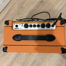 Kytarový kombo zesilovač s oranžovým povrchem a bílým ovládacím panelem. Na přední straně je nápis ORANGE CRUSH 20 a řada ovládacích knoflíků s popis…