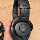 Černé uzavřené sluchátka s polstrovaným náhrobkem. Na vnější straně mušle je kulaté logo a nápis AUDIO-TECHNICA. Na horní části náušníku je viditelné…