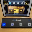 Černý MIDI kontrolér iRig BlueBoard se čtyřmi bílými tlačítky označenými písmeny A, B, C a D. Tlačítko A svítí modře. Nad ním je tablet s aplikací, k…