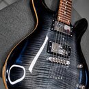 Elektrická kytara s tmavým, žilnatým povrchem těla a hnědým hnedlecem. Nástroj má dva humbuckery, fixační most a tři ovládací knoflíky. Na těle nejso…