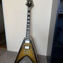 Elektrická kytara s typickým V-tvarem těla v žlutém gradientním provedení s černým okrajem. Na hlavě je viditelné logo Gibson. Kytara má dva humbucke…
