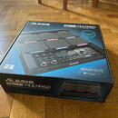 Krabice s produktem Alesis STRIKE MULTIPAD, popsaným jako PERCUSSION PAD WITH SAMPLER AND LOOPER. Na obalu je zobrazen černý perkusní pad s podsvícen…