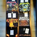 Šest černých triček s potisky hudebních kapel rozložených na hnědém povrchu. Jsou zde trička s nápisy METALLICA (dvě různá grafiky), ACCEPT, QUEENS O…