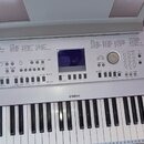 Stříbrný digitální klavír značky YAMAHA. Na ovládacím panelu jsou viditelné nápisy „SONG“, „STYLE“, „VOICE“ a „MUSIC DATABASE“ spolu s rozsáhlými sez…
