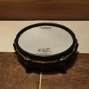 Černý elektronický buben s bílou membránou a chromovaným obručem. Na membráně jsou nápisy Roland MESH HEAD made by REMO a V-Drums. Dole je drobný tex…