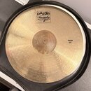 Zlatý činel s koncentrickým žilováním, umístěný v černém obalu. Na povrchu je bílý štítek s nápisy pAiste, Twenty a TRADE MARK MADE IN SWITZERLAND. V…