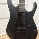 Černá elektrická kytara s matným povrchem. Nástroj má dva humbuckery, jeden ovládací knoflík hlasitosti a přepínač zvuků. Na těle nejsou žádná vidite…