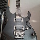 Tmavě šedá elektrická kytara s kovovými stupnicemi a třemeným mostem. Na hlavě hředu je viditelné logo Ibanez. Tělo kytary má třpytivý povrch a dvě o…