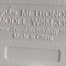 Detail bílého plastového povrchu s vyraženým textem. Je zde uveden název cherub METRONOME, MODEL: WSM-330 a webová adresa www.cherubtechnology.com. D…